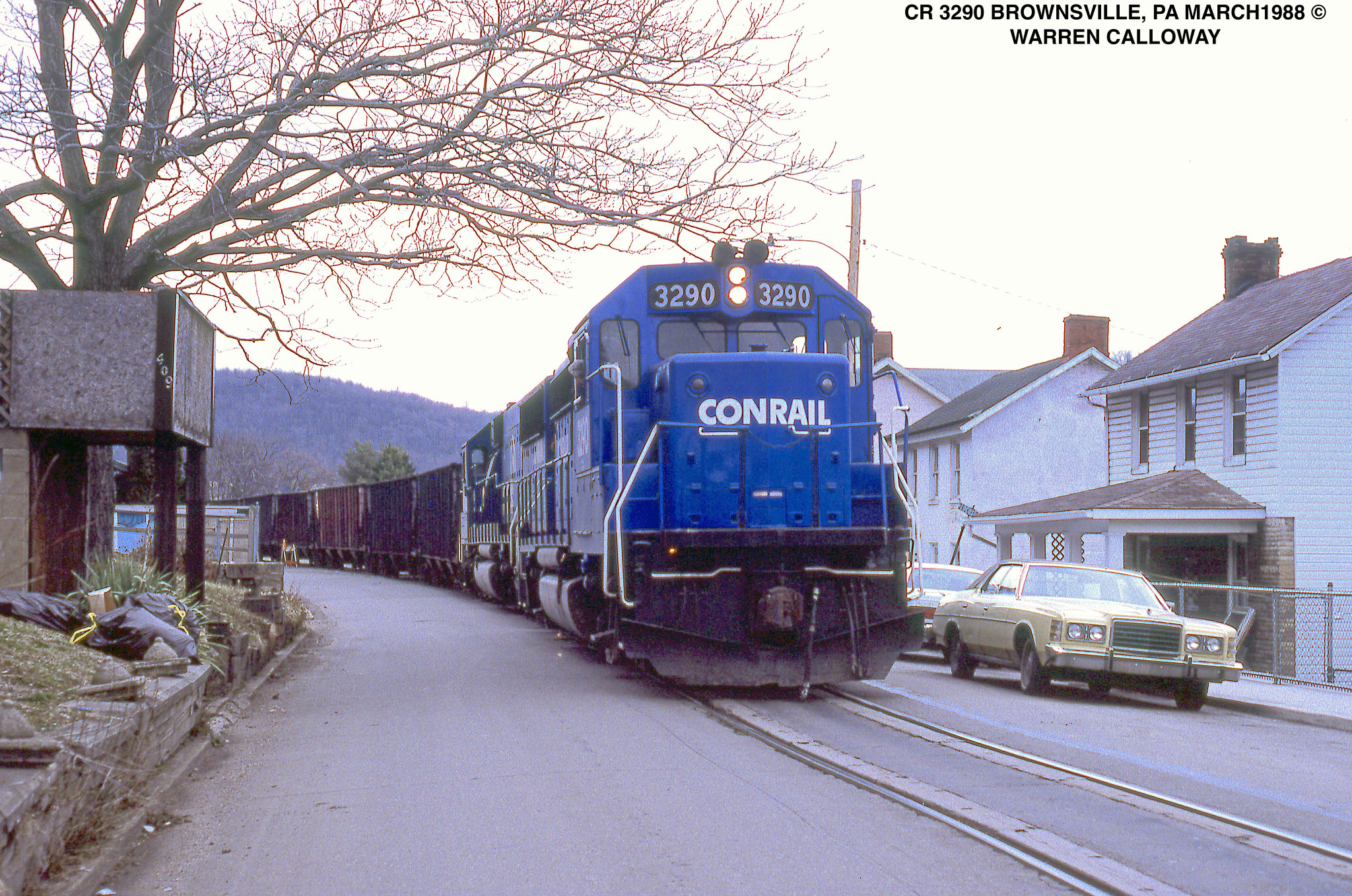 Conrail GP40-2 3290 leads empty hoppers through street running in Brownsville Pennsylvania in March 1988